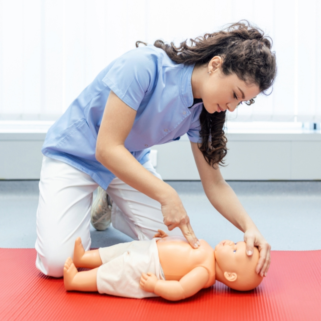 Instructor demonstrating infant CPR on a training manikin, representing hands-on First Aid and CPR training for childcare providers to ensure safety and emergency preparedness.