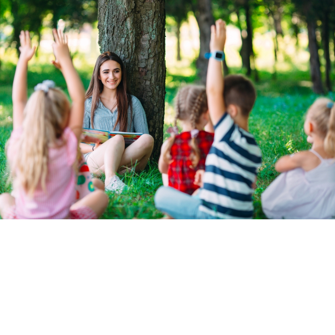 Outdoor classroom scene in Tehama or Shasta County – teacher reading to young children, students raising hands during interactive early education activity, promoting CPR and First Aid training for childcare providers and schools.