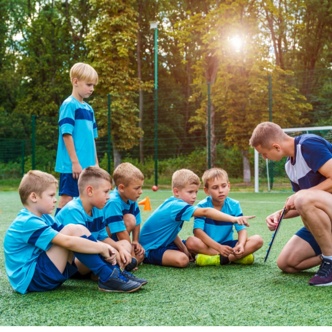 Coach and young soccer players joining hands in a team huddle. Promoting safety and emergency preparedness for camps, youth sports leagues, and community organizations through First Aid and CPR training.