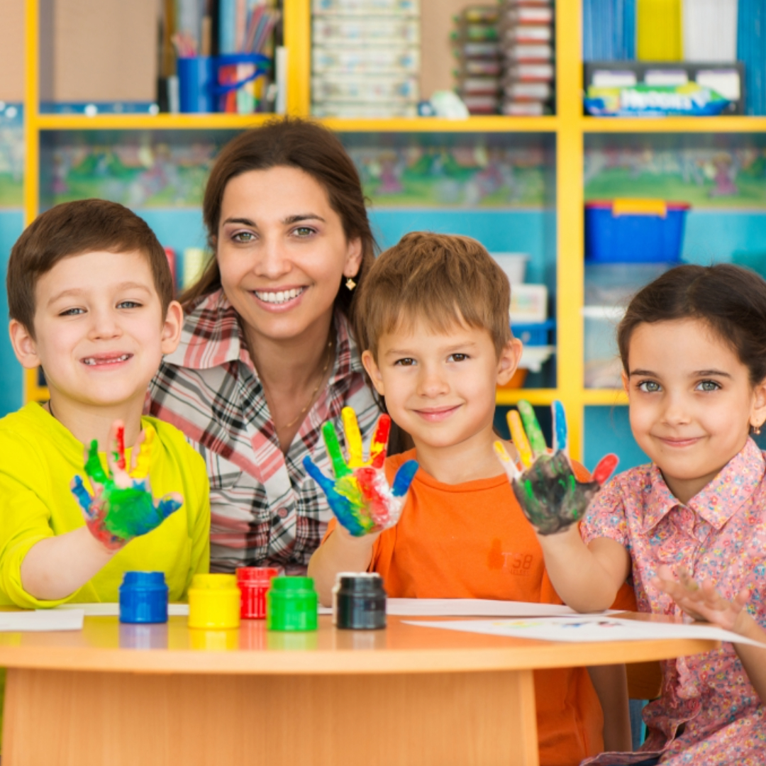 Child care provider smiling with preschool children showing painted hands during a classroom activity, highlighting early education and child development
